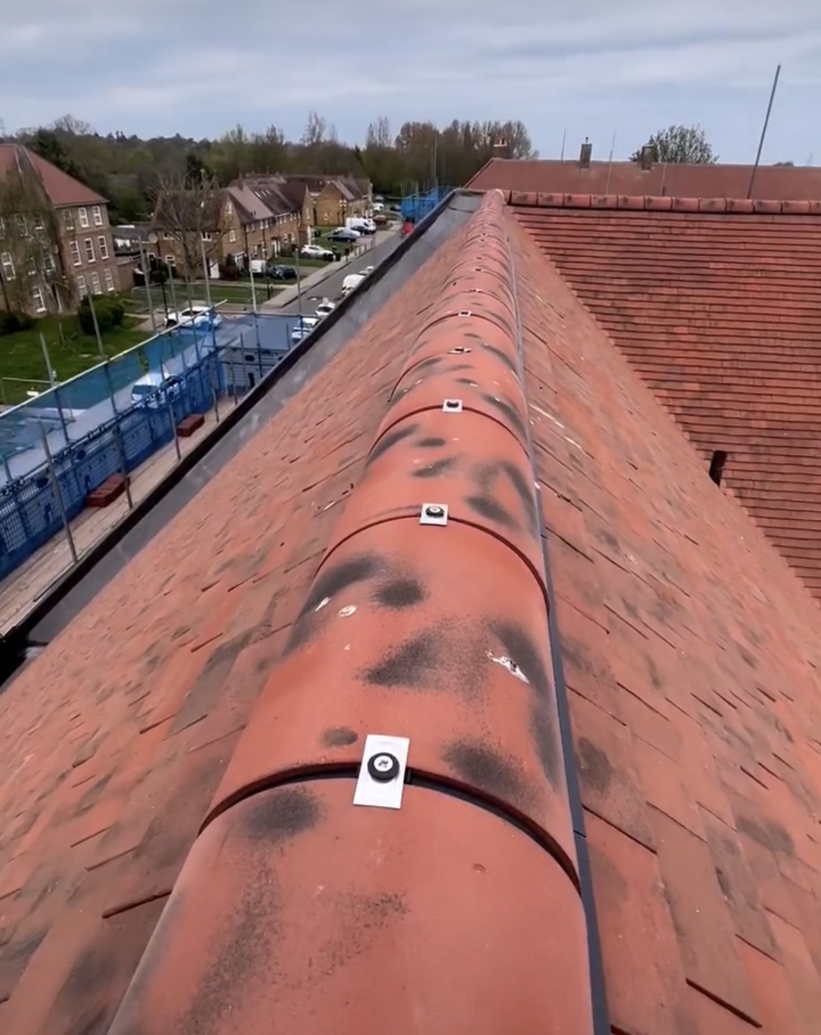 Mechanically fixed red ridge tiles on a plain tiled roof