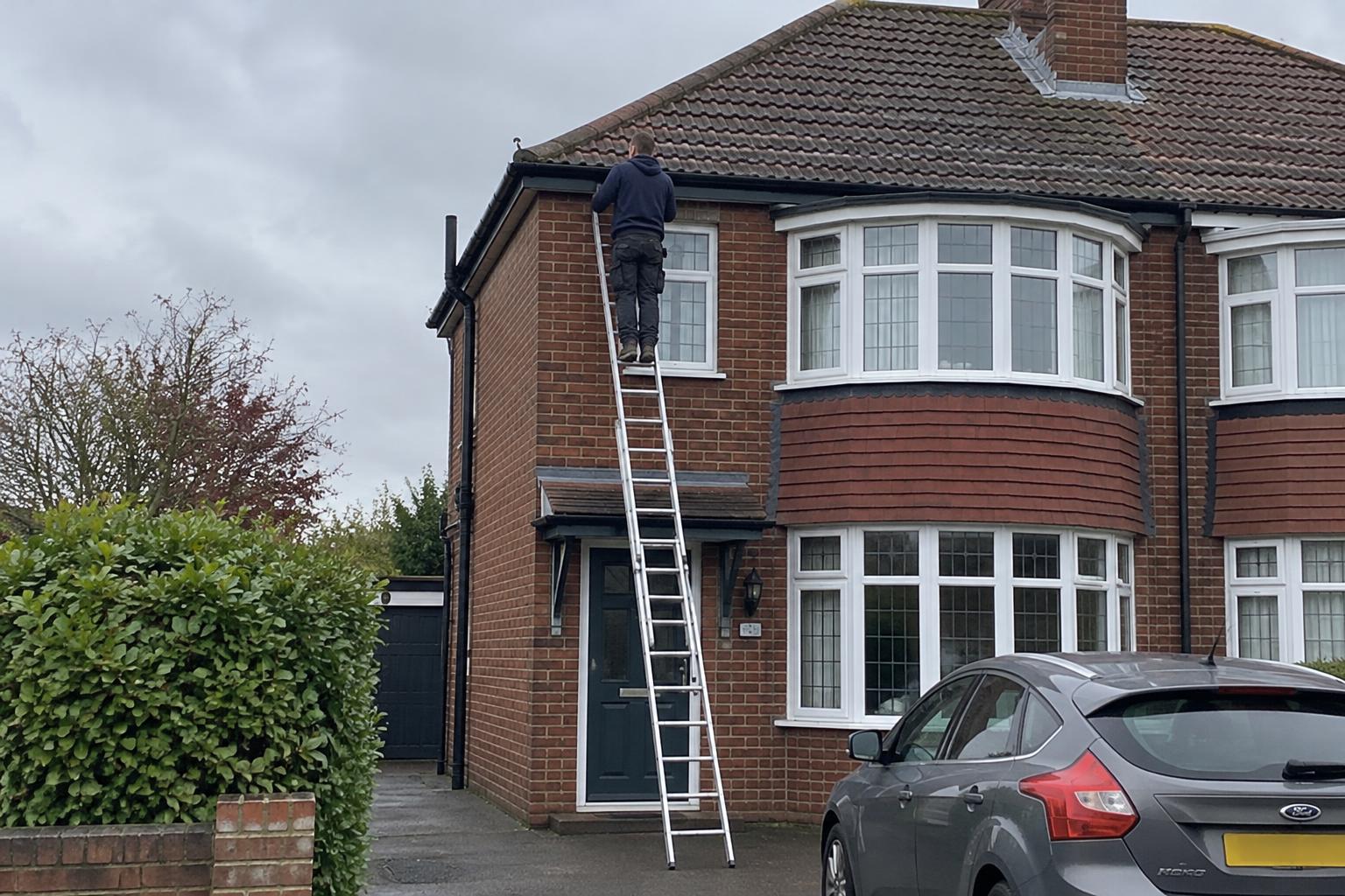 Roofer on a ladder photographing a slate roof during a survey