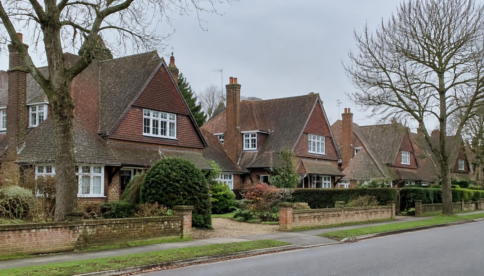 Arts and Crafts style detached houses with steep red-brown plain clay tile roofs and tile-hung gables on a tree-lined street